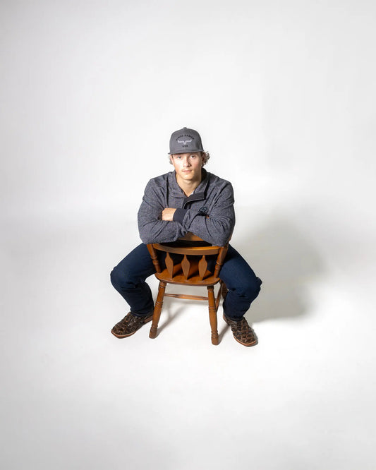 Tyson, is wearing Kimes Ranch flees sweater with a Kimes Ranch trucker hat in grey, Kimes ranch Watson jeans and Durango pirarucu boots